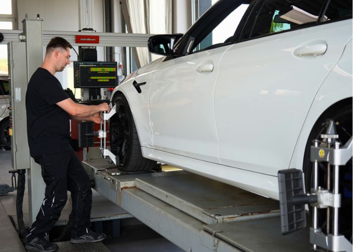 Mitarbeiter führt in der Kfz-Werkstatt eine Achsvermessung durch.